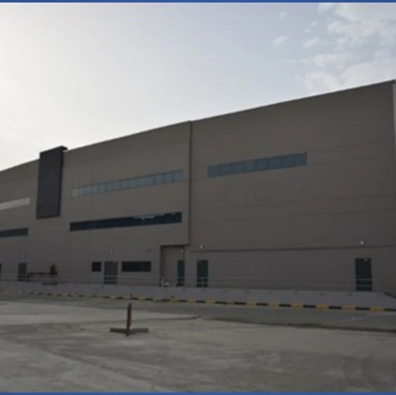 A broad industrial façade with service access and a paved forecourt.