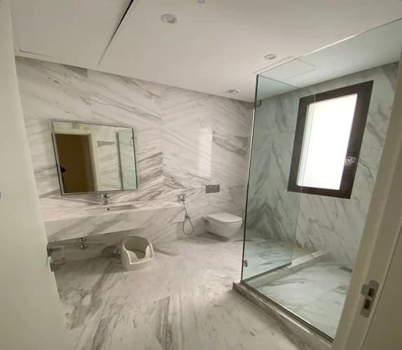 Veined wall and floor finishes with a glass shower enclosure and fitted vanity.