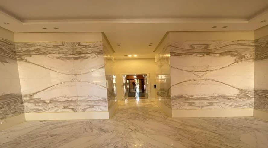 Large-format veined stone surfaces and recessed ceiling lighting.