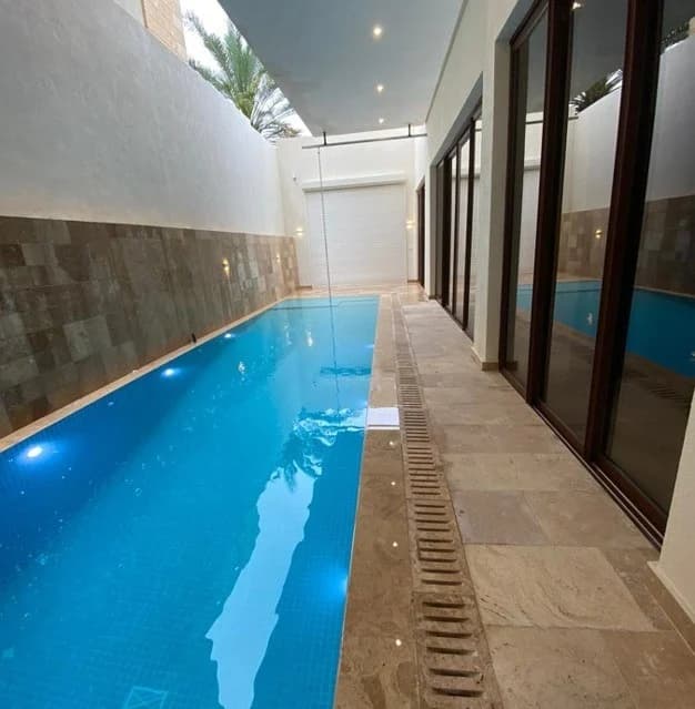 An elongated pool bordered by stone finishes and full-height glazed openings.